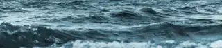 Blurred choppy sea waves under a calm sky at dusk, with the horizon glowing subtly, conveying a sense of tranquility and the vastness of the ocean.